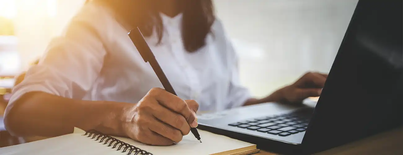 Person writing while on laptop