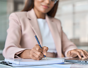 Woman writing on paper and looking at laptop